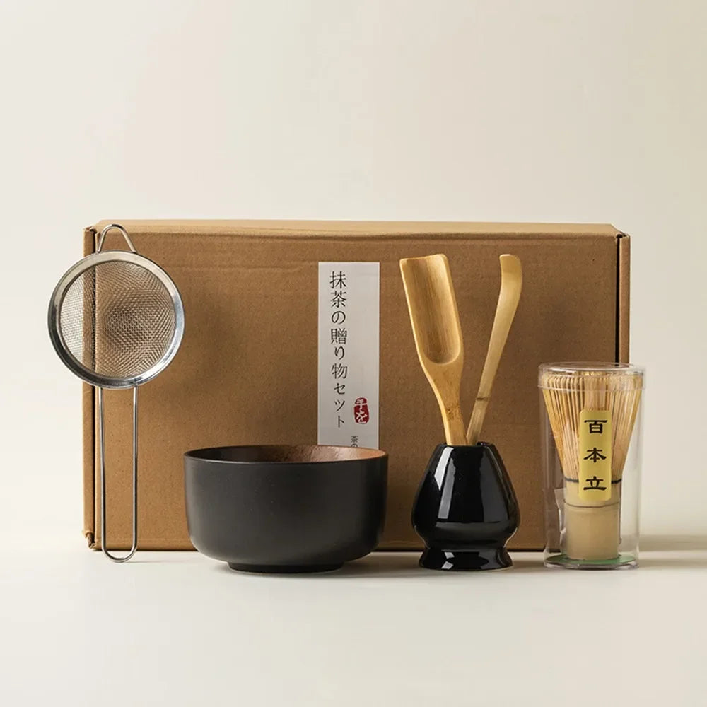 Matcha tea kit with matte black ceramic bowl bamboo whisk scoop whisk holder and strainer placed in front of a gift box