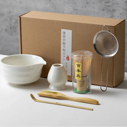 Set of white tea-making tools with a cardboard box on a gray background