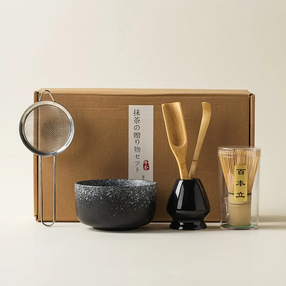 Matcha tea gift set with black ceramic bowl bamboo whisk scoop strainer and whisk holder placed in front of a gift box