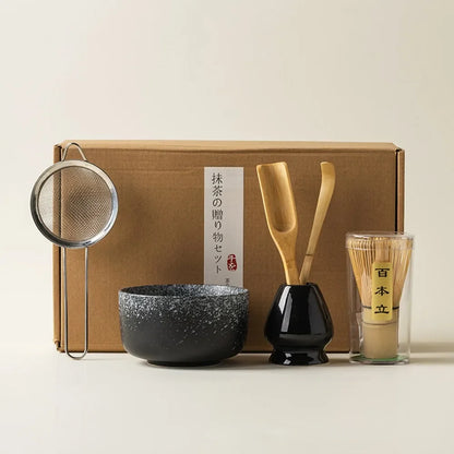 Matcha tea gift set with black ceramic bowl bamboo whisk scoop strainer and whisk holder placed in front of a gift box