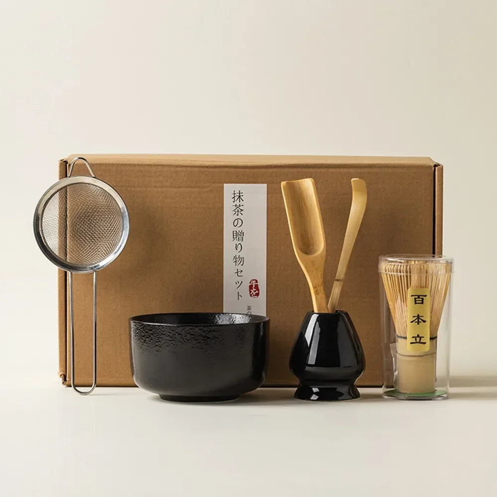 Matcha tea kit with glossy black ceramic bowl bamboo whisk scoop strainer and whisk holder in front of a gift box