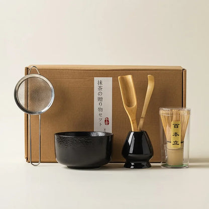 Matcha tea kit with glossy black ceramic bowl bamboo whisk scoop strainer and whisk holder in front of a gift box