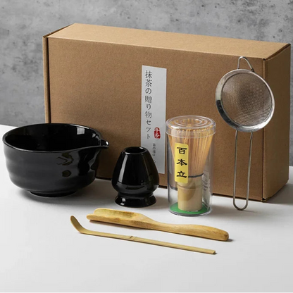 Tea-making set with black bowl, whisk, scoop, and other tools in front of a cardboard box labeled '6PCS - Black'.