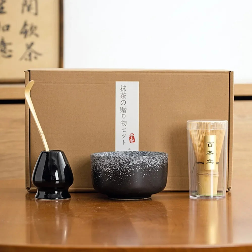Matcha tea kit with black ceramic bowl bamboo whisk scoop and black whisk holder in front of a gift box