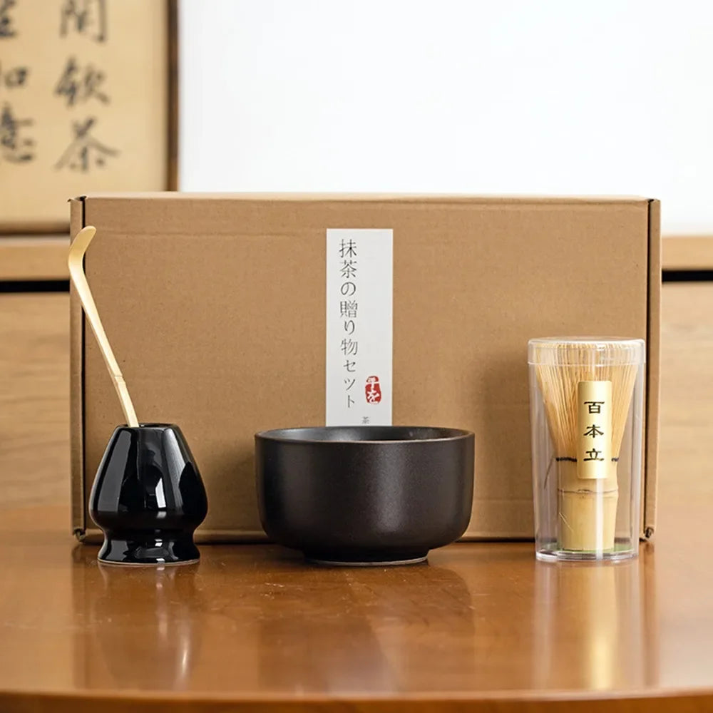 Matcha tea kit with black ceramic bowl bamboo whisk scoop and whisk holder arranged in front of a gift box