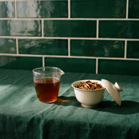 Brewed Dianhong black tea in a glass, deep amber red, beside a gaiwan of wet leaves