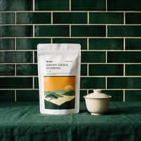 Golden Needle Dianhong pouch beside a white gaiwan on a green cloth