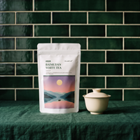 Bai Mu Dan white tea pouch beside a white gaiwan on a green cloth